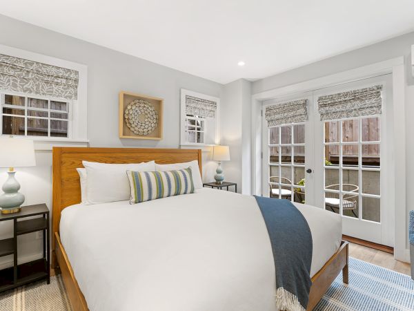 A cozy bedroom with a large bed, decorative pillows, lamps, art on the wall, and patio doors leading outside.