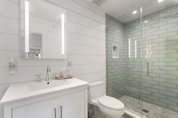 A modern bathroom with a glass shower, white sink, illuminated mirror, and a toilet in a clean, minimalist style.