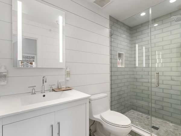 A modern bathroom with a glass shower, white sink, illuminated mirror, and a toilet in a clean, minimalist style.