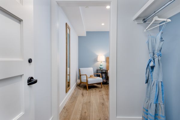 The image shows an open door leading to a cozy room with a blue accent wall, a chair, a lamp, and a dress hanging in a closet on the right side.