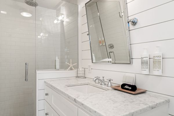 A modern bathroom with a marble countertop, wall-mounted toiletries, and a glass shower enclosure.