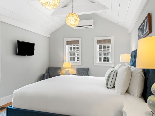 A cozy bedroom with a large bed, two chairs, lamps, a wall-mounted TV, and a sign reading "Nantucket".