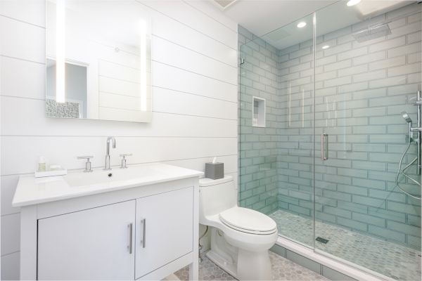 A modern bathroom with a glass-enclosed shower, white vanity with a mirror, toilet, and sleek fixtures in white and silver finishes.