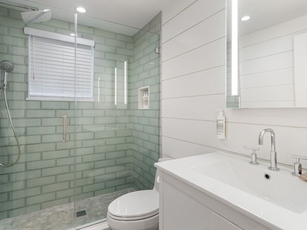 A modern bathroom features a glass shower with green tiles, a white sink, and a toilet, all under bright lighting.