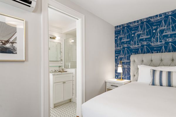 A modern bedroom with a blue nautical-themed accent wall, framed boat picture, and attached bathroom featuring a white vanity and shower.