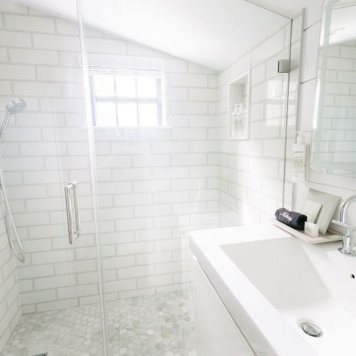 Bright modern bathroom with tiled walls, a glass walk-in shower, rainfall showerheads, and a white sink vanity.