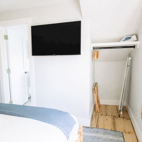 Bright bedroom with a wall-mounted TV, open door, and cleaning tools on the floor beside a window.