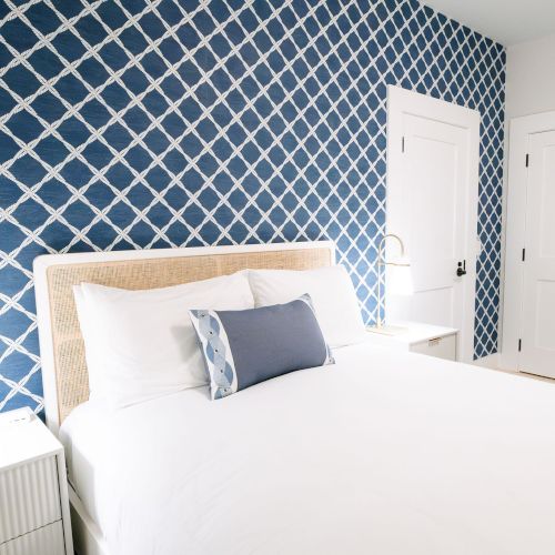 A bright bedroom with a blue lattice-pattern wall, a neatly made bed, side table lamp, and white closet doors.