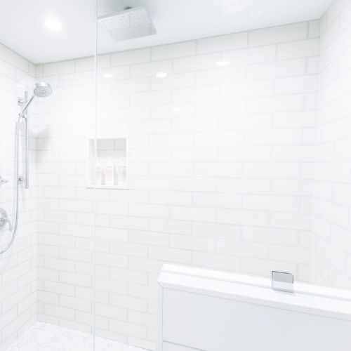 A bright modern shower with chrome rain showerhead and tiled walls in a clean white bathroom.