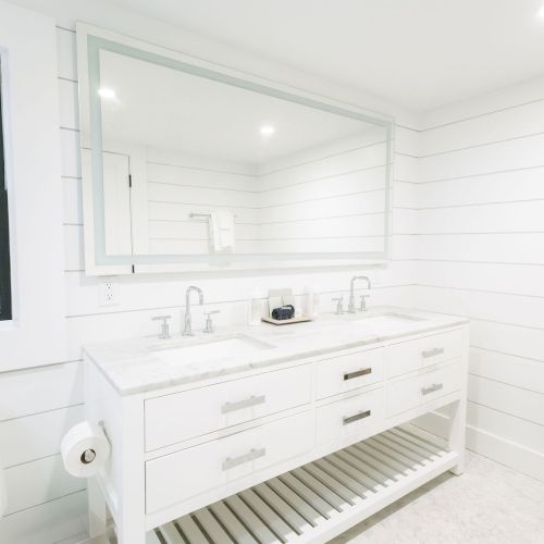 Bright modern bathroom with a double marble sink vanity, wall mirror, chrome faucets, and white tiled walls.