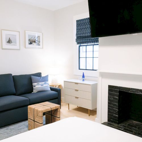 A bright living room with a dark sofa, framed sailboat photos, a TV, a window, and a white mantel fireplace.