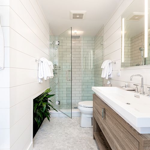 A modern bathroom with a glass-enclosed shower, double sink vanity, white tiles, and a hanging robe on the wall.