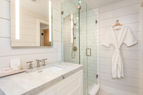 A modern bathroom features a marble countertop vanity, a glass-enclosed shower, and a white bathrobe hanging on the wall.