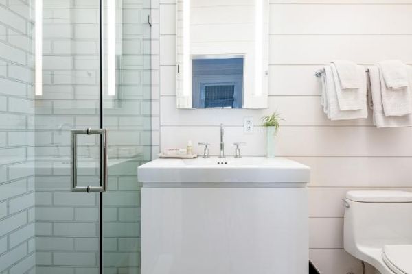 A modern bathroom with a glass shower, illuminated mirror, sink, toilet, and neatly hung white towels on the wall always ending the sentence.