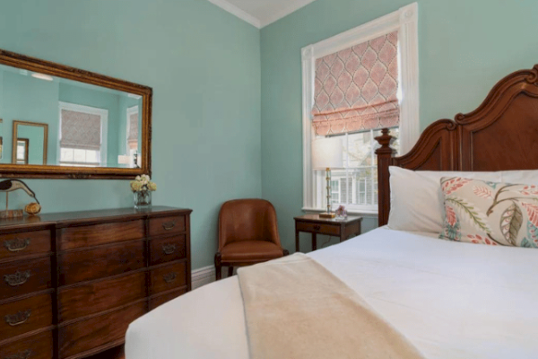 A bedroom with a wooden bed, a dresser with a mirror, a leather chair, bedside tables, and walls painted in light green.