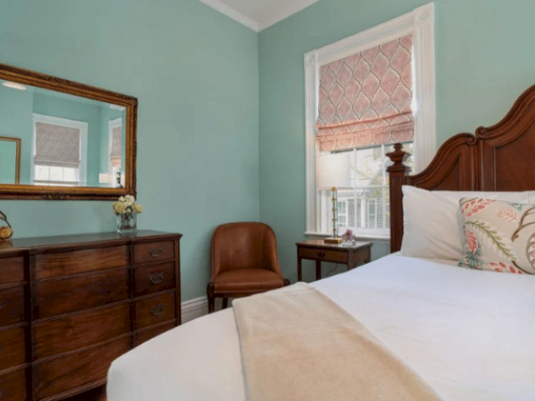 A bedroom with a wooden bed, a dresser with a mirror, a leather chair, bedside tables, and walls painted in light green.