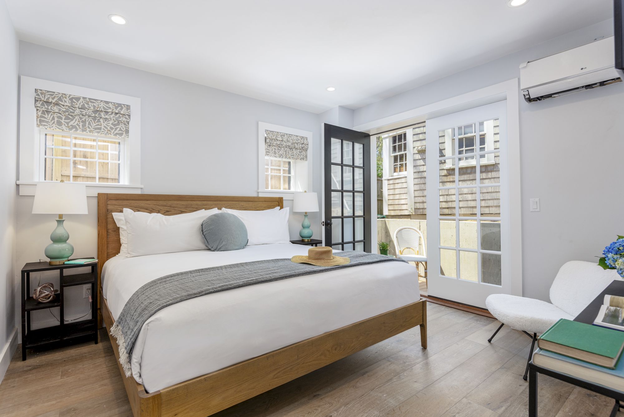 A modern bedroom with a wooden bed, two nightstands with lamps, a chair, and French doors leading to an outdoor area.