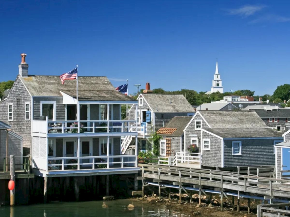 The image shows a quaint seaside village with wooden houses, American flags, a pier, and a white church tower in the background.