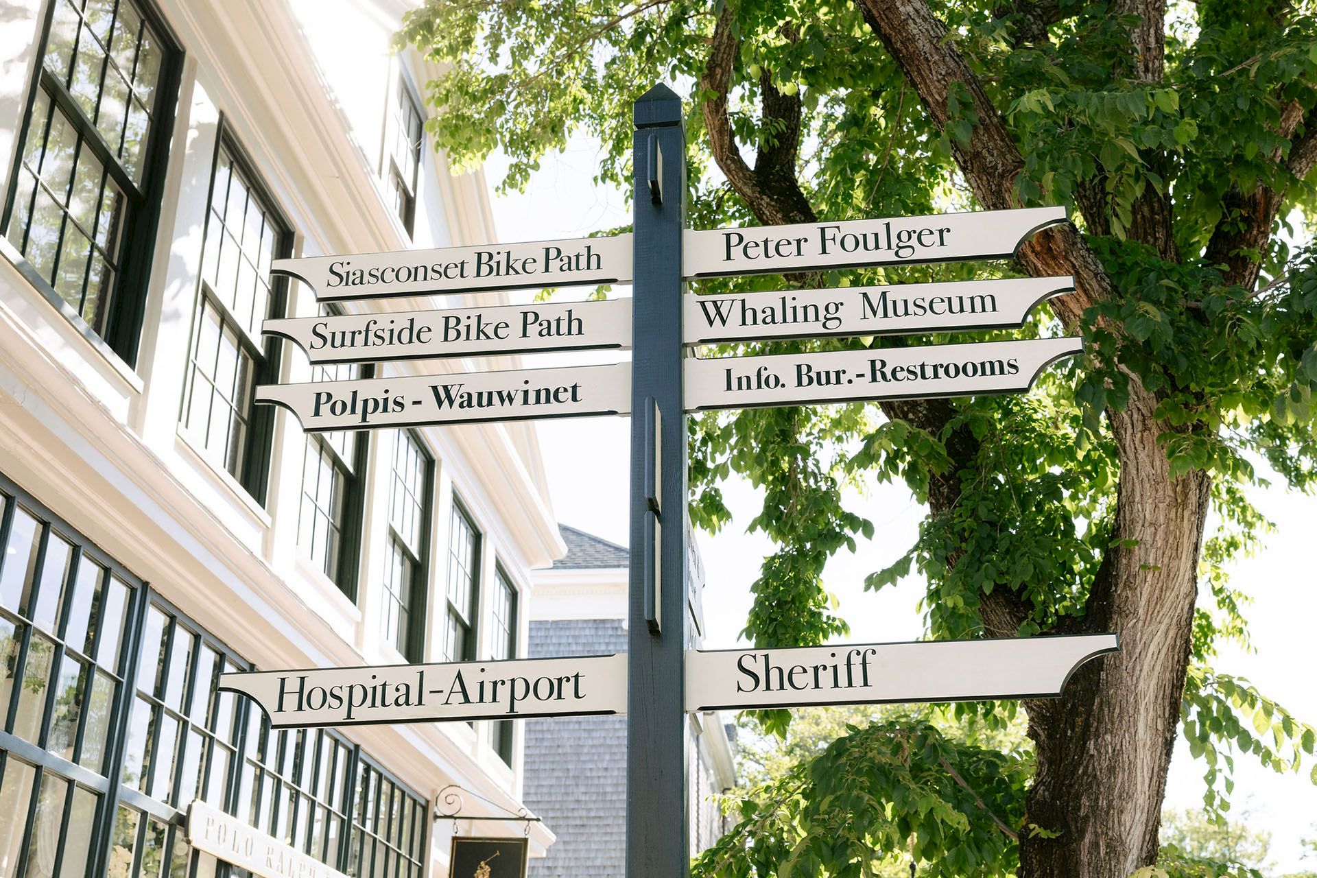A green street sign post in a park lists directions to places like Siasconset Bike Path, Surfsid Bike Path, Whaling Museum, and more.