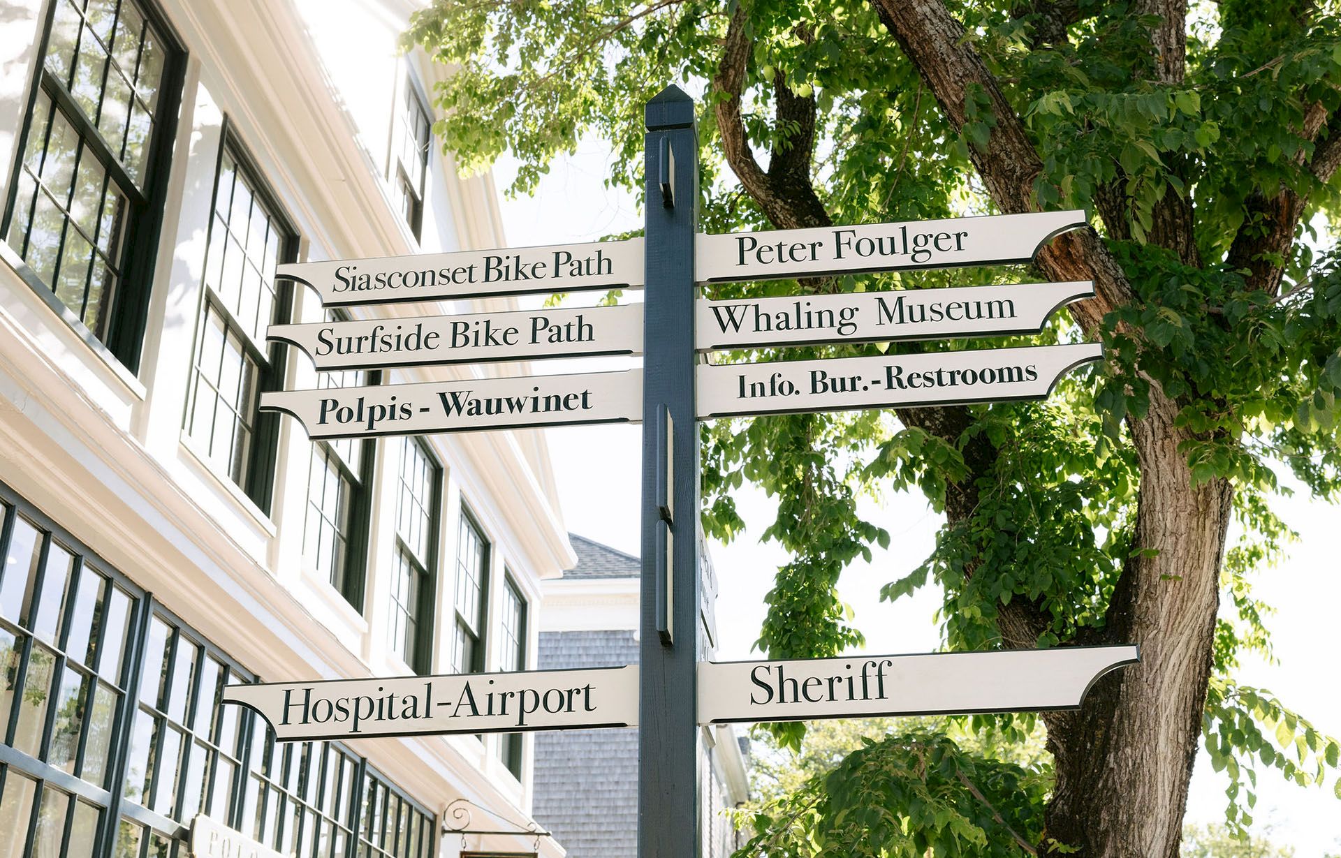 A green street sign post in a park lists directions to places like Siasconset Bike Path, Surfsid Bike Path, Whaling Museum, and more.