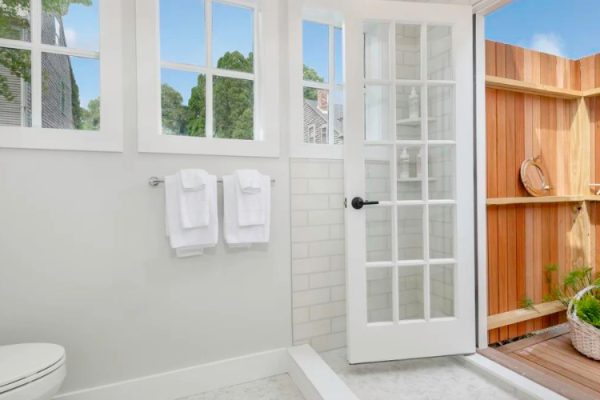 A bright bathroom with white towels, large windows, a glass door leading to an outdoor wooden deck with plants and decor.