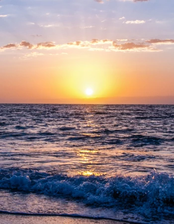 A beautiful sunset over the ocean with waves gently crashing onto the shore, and a colorful sky with clouds and reflections on the water.