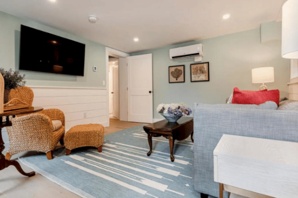 A cozy living room with wicker chairs, a TV on the wall, a sofa, a rug, a side table, a coffee table, and wall art, in a bright, modern setting.