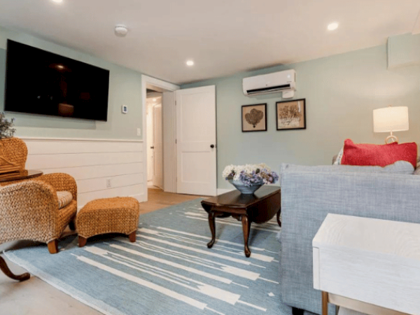 A cozy living room with wicker chairs, a TV on the wall, a sofa, a rug, a side table, a coffee table, and wall art, in a bright, modern setting.