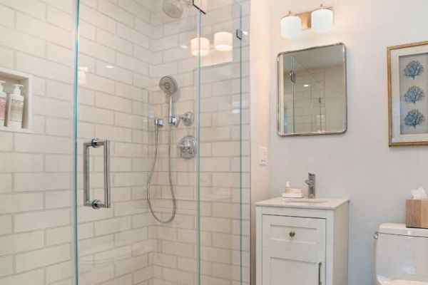 Modern bathroom with a glass shower, white subway tiles, a small vanity with a mirror, wall-mounted lights, art, and a toilet with a tissue box.