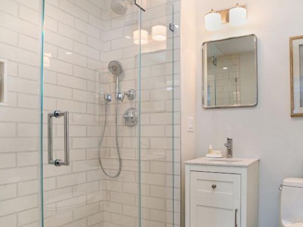 Modern bathroom with a glass shower, white subway tiles, a small vanity with a mirror, wall-mounted lights, art, and a toilet with a tissue box.