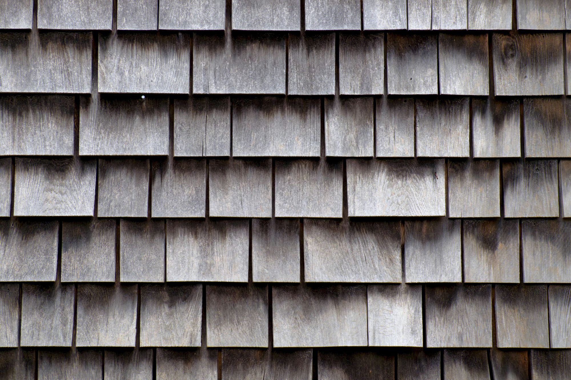 The image shows a close-up of a wall with wooden shingles, arranged in overlapping rows to create a textured surface.