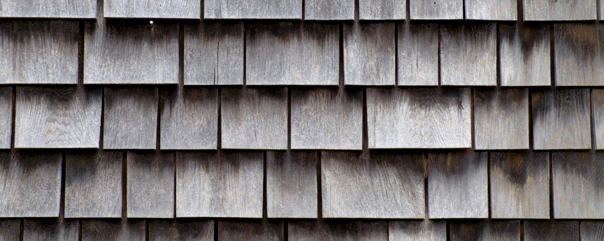 A close-up of weathered gray wooden shingles forming a textured roof pattern.