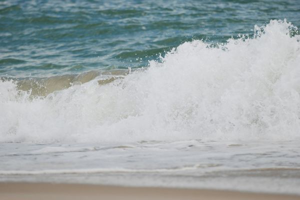 Waves are crashing onto a sandy beach, creating white foam and turbulence in the water in this coastal scene.