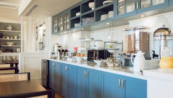 A kitchen setup with blue cabinets, breakfast items, and dispensers. Dishes and cereal are on display in a cozy, modern space.