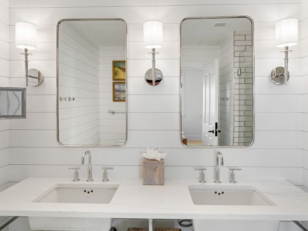 A modern bathroom with double sinks, two mirrors, wall lamps, and a tissue box on a marble countertop.