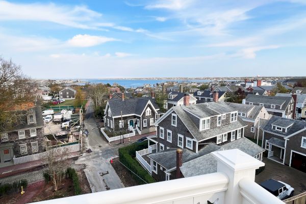 A scenic view of a coastal neighborhood with charming houses, a clear blue sky, and ocean in the background.