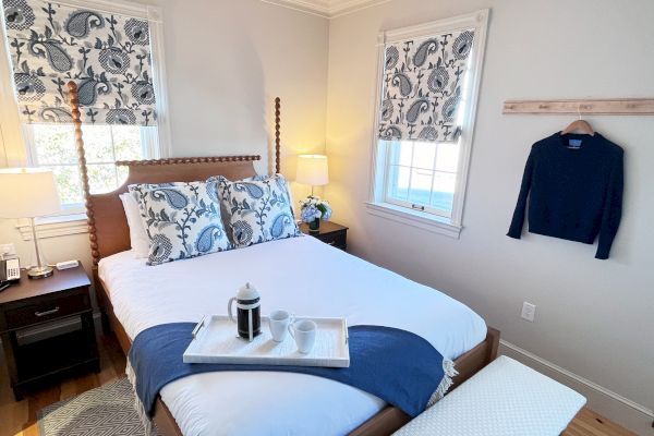 A cozy bedroom with patterned curtains, a bed with decorative pillows, a tray with coffee, and a sweater hanging on the wall.