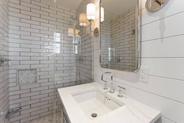 A modern bathroom with white subway tiles, a large mirror, a sink with a faucet, wall lights, and a glass shower enclosure ends the sentence.