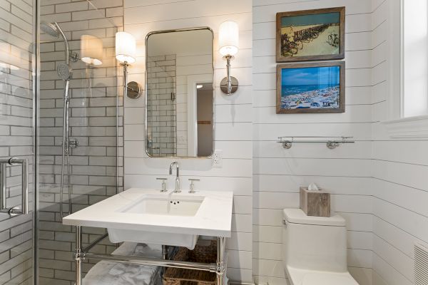 This image shows a modern bathroom with a mirror, sink, and toilet. There are framed pictures and wall lights, creating a cozy ambiance.