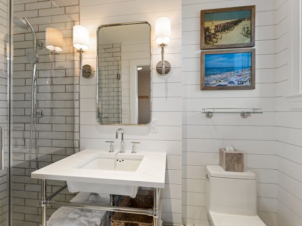 This image shows a modern bathroom with a mirror, sink, and toilet. There are framed pictures and wall lights, creating a cozy ambiance.