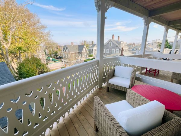 A porch with wicker furniture overlooks a scenic neighborhood, featuring charming houses and a clear blue sky.