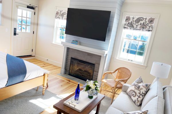 A cozy living room with a fireplace, wall-mounted TV, couch, coffee table, and windows, all in a bright and airy setting.