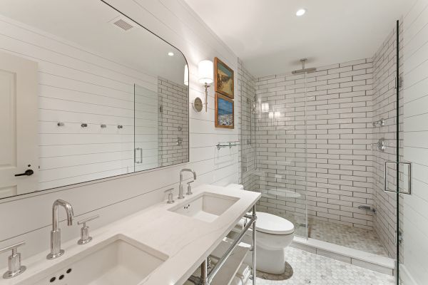 The image shows a modern bathroom with a double sink, large mirror, shower with glass doors, and white subway tiles throughout the space.