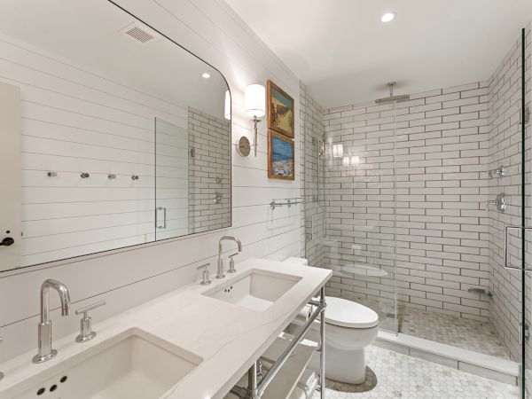 The image shows a modern bathroom with a double sink, large mirror, shower with glass doors, and white subway tiles throughout the space.