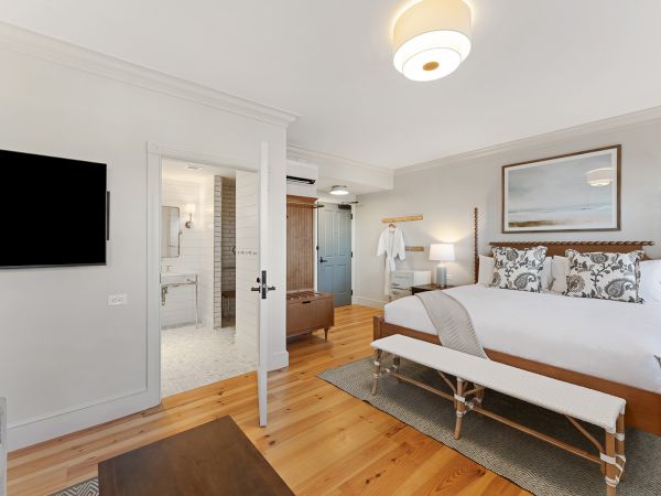 A modern bedroom with a large bed, a TV on the wall, an open door revealing a bathroom, and a cozy atmosphere.