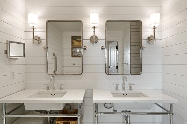 The image shows a bright bathroom with two vanities, wall mirrors, and lights above each sink, set against white paneled walls.