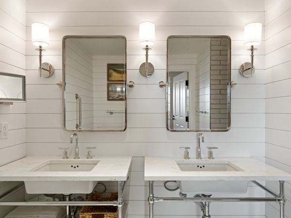 The image shows a bright bathroom with two vanities, wall mirrors, and lights above each sink, set against white paneled walls.