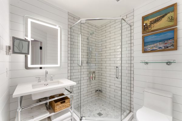 A modern bathroom with a glass shower, illuminated mirror, white sink, and wall art. The decor is sleek and uses a light color palette.