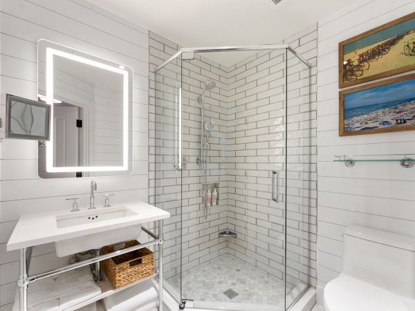 A modern bathroom with a glass shower, illuminated mirror, white sink, and wall art. The decor is sleek and uses a light color palette.