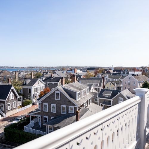 A coastal town with charming houses and a view of the ocean, seen from a porch with a white balustrade under a clear sky.